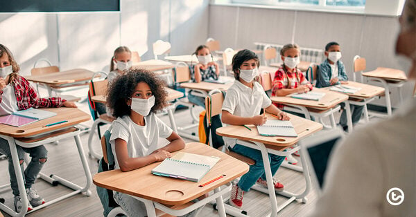 little boy wearing a mask gets a temperature screening at school